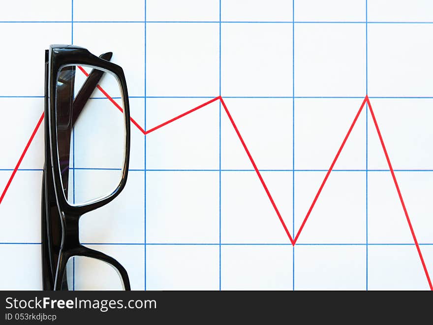 Business concept. Eyeglasses lying on paper background with red chart. Business concept. Eyeglasses lying on paper background with red chart