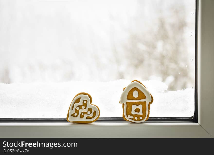 Gingerbread cookies in shape of house and heart on the winter window. Concept for christmas loneliness and sadness. Gingerbread cookies in shape of house and heart on the winter window. Concept for christmas loneliness and sadness