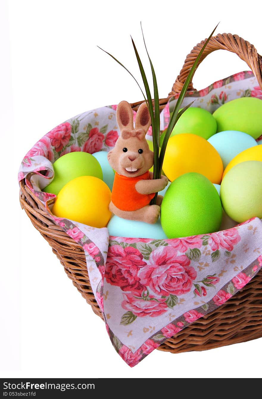 Easter bunny sitting in a basket with colored eggs and holding green leaves. Isolated on a white background. Easter bunny sitting in a basket with colored eggs and holding green leaves. Isolated on a white background.