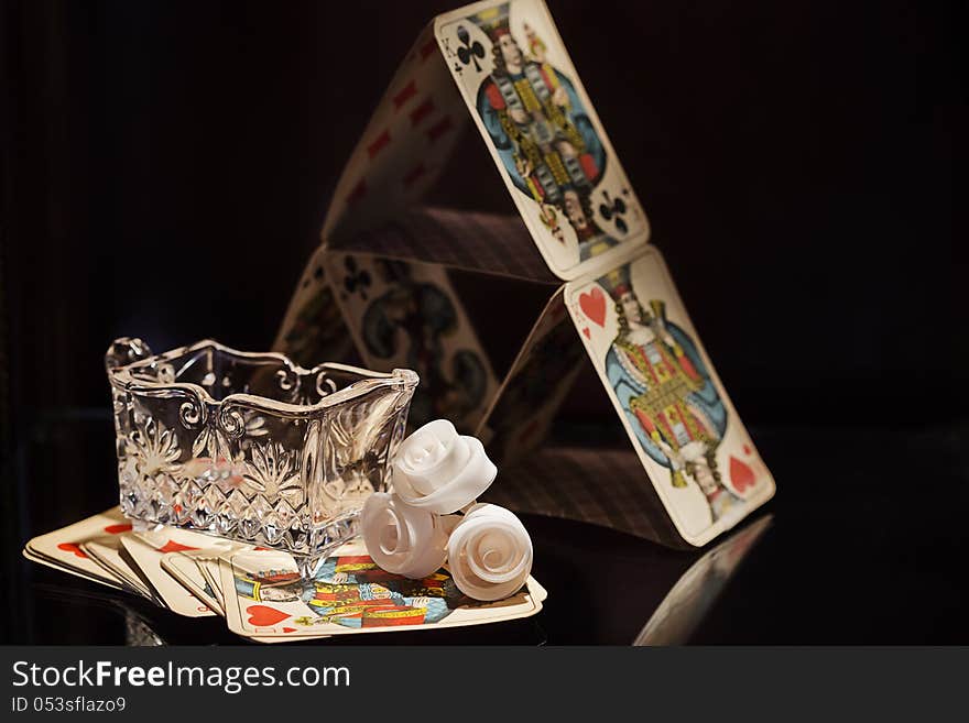 Small crystal sugar cup, some wax roses and a pyramid of playing cards.