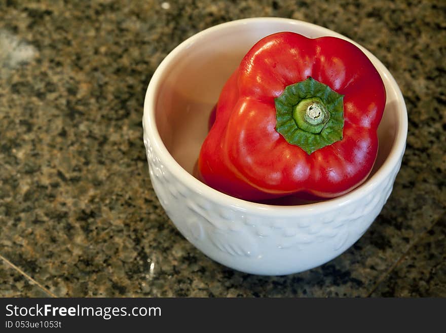 Red bell pepper in a white bowl on a granite countertop. Red bell pepper in a white bowl on a granite countertop.