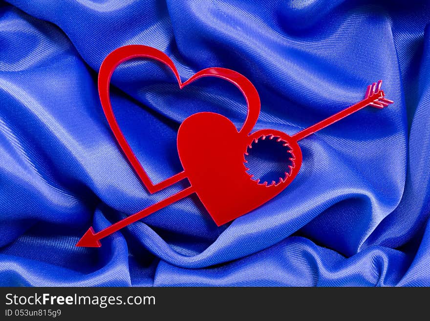 Two love hearts shapes with arrow and cogwheel hole inside of one of them on a blue silk background. Two love hearts shapes with arrow and cogwheel hole inside of one of them on a blue silk background