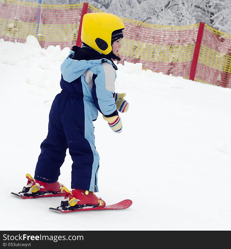Small child with yellow skiing helmet learning to ski in a winter sport resort. Small child with yellow skiing helmet learning to ski in a winter sport resort.