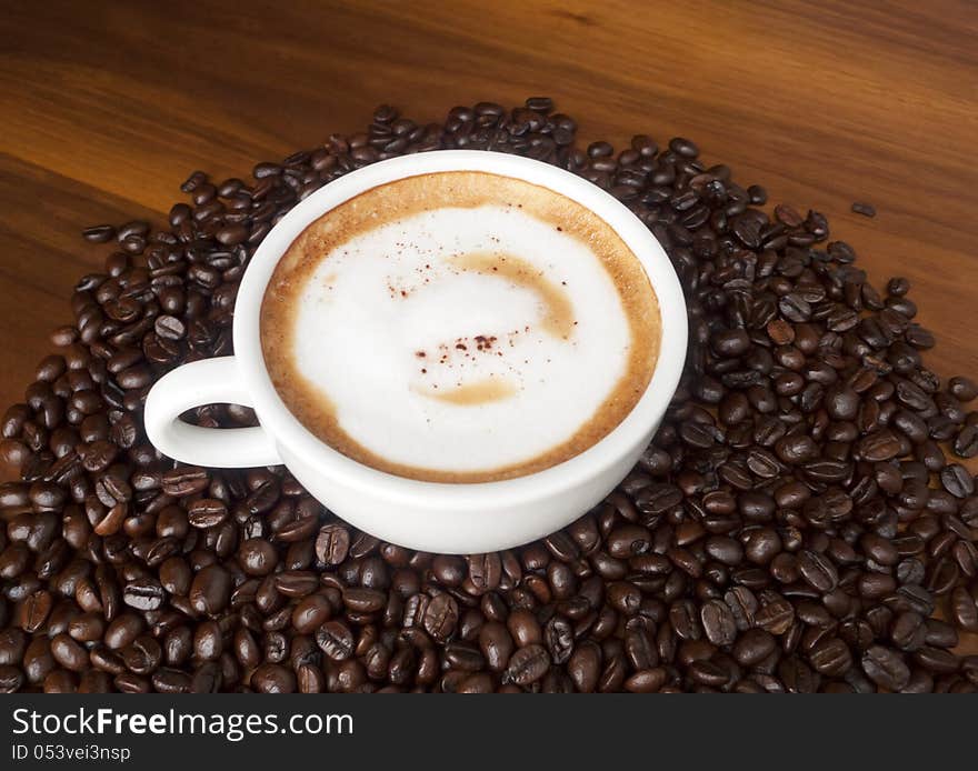 Coffee cup in an environment of Coffee beans on the wood. Coffee cup in an environment of Coffee beans on the wood