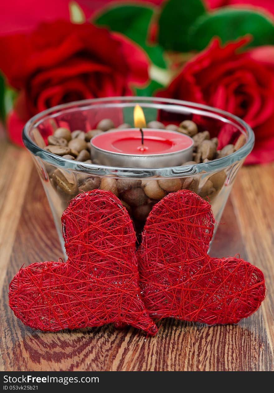 Red candle in a glass cup with coffee beans and two hearts for Valentine's Day closeup