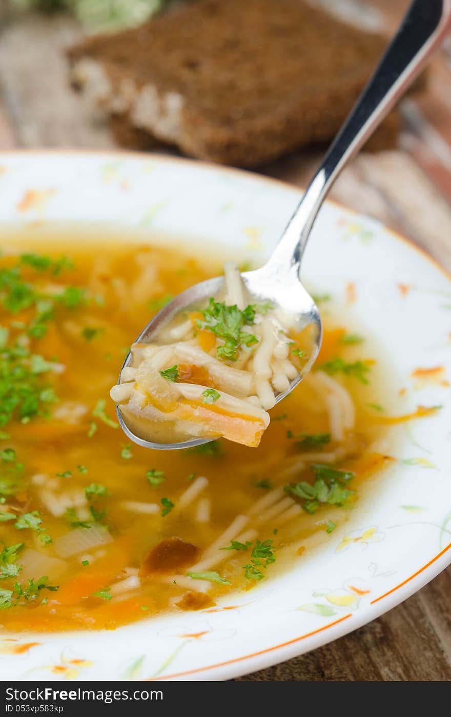 Spoon of chicken soup with noodles and carrots closeup vertical