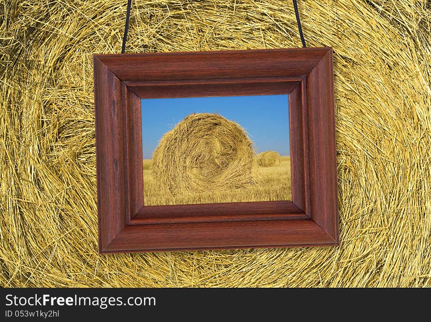 Picture in wooden frame hanging on the background stack of hay. Picture in wooden frame hanging on the background stack of hay