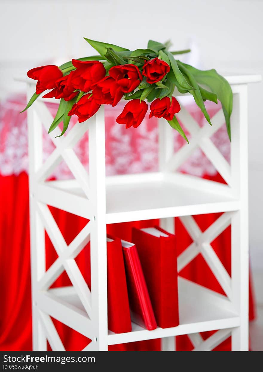 Red tuplips lying down on a white stand with books. Red tuplips lying down on a white stand with books