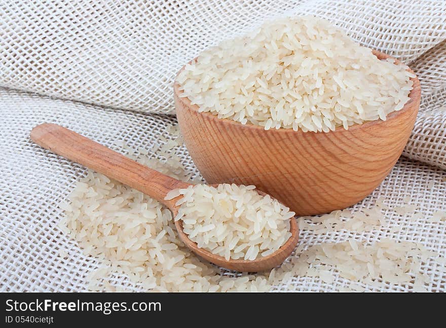 Raw white rice in wooden bowl and spoon on burlap, food ingredient photo