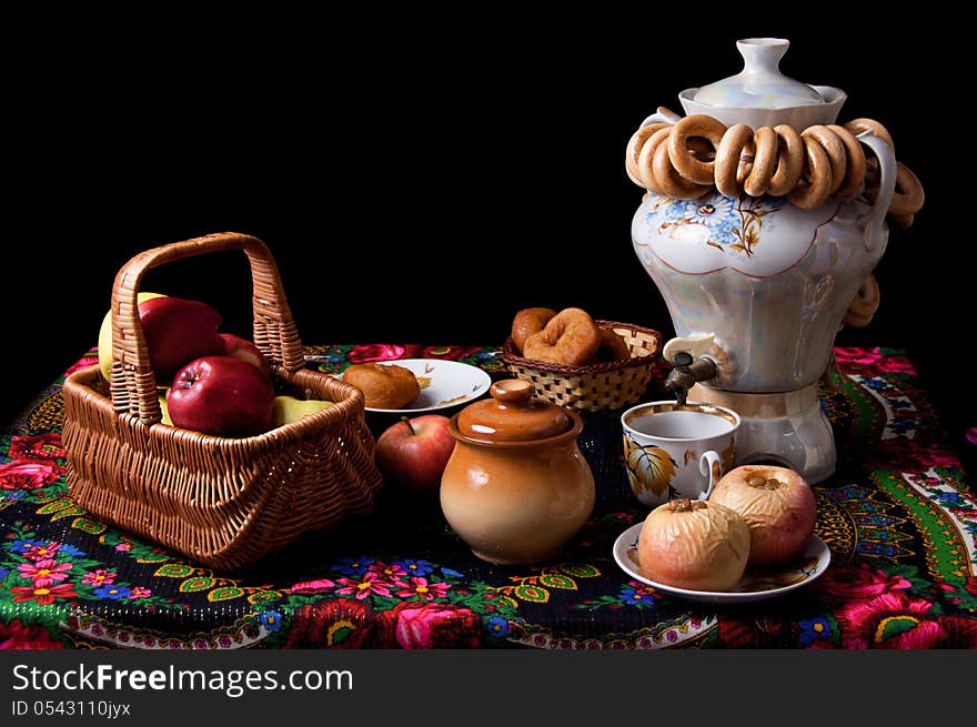 Samovar, bagels and apples on table over black