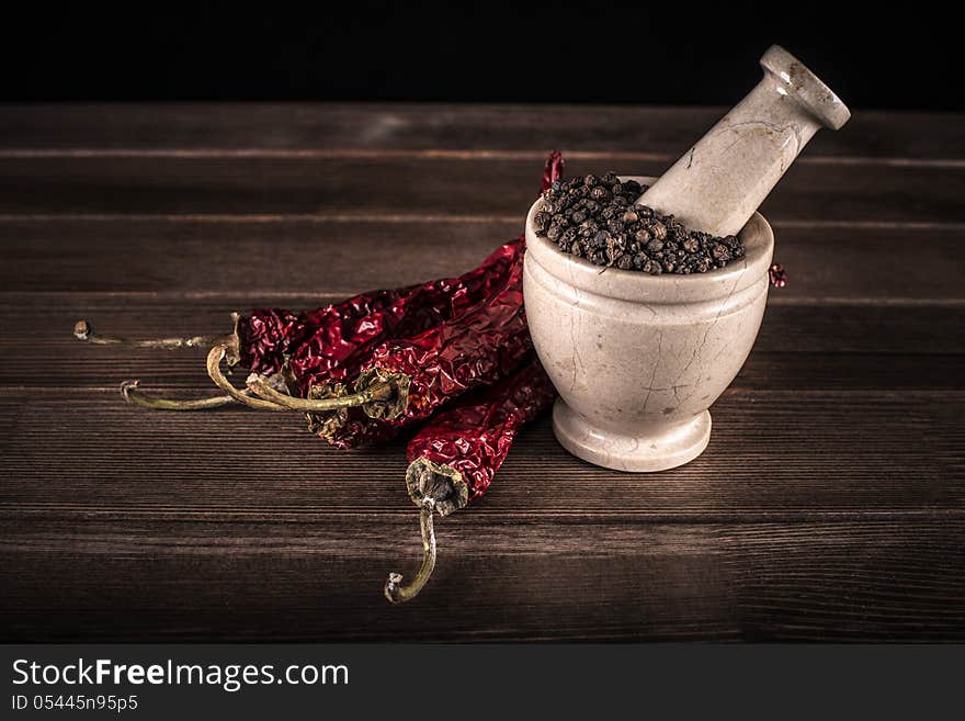 Marble mortar with spices black pepper and red hot pepper on a wooden table