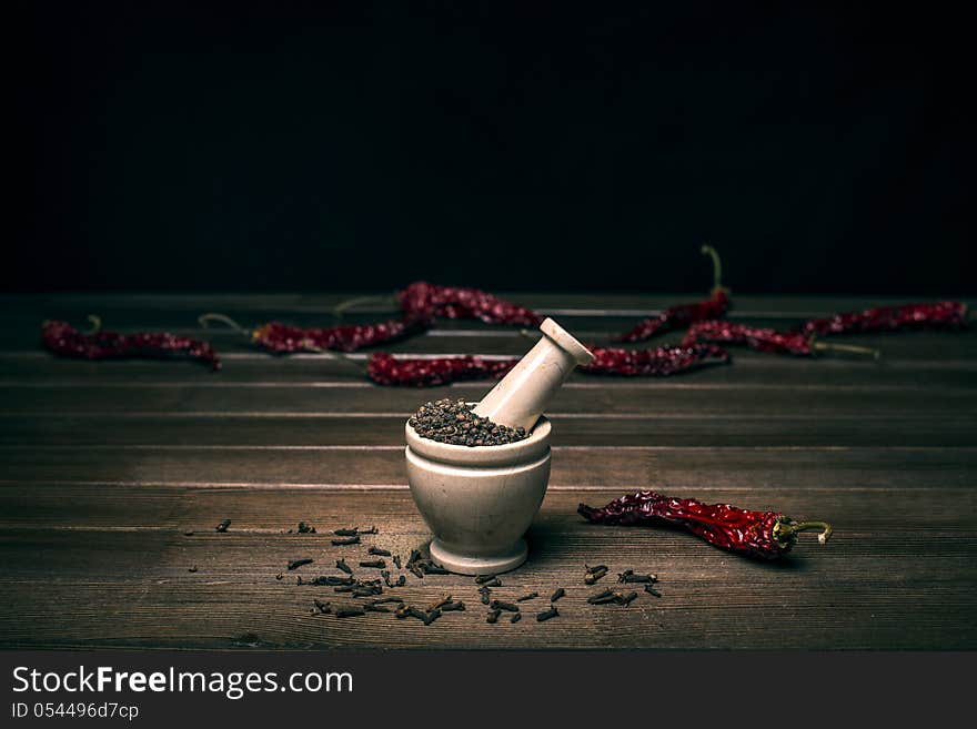 Marble mortar with spices black pepper, carnation and red hot pepper on a wooden table