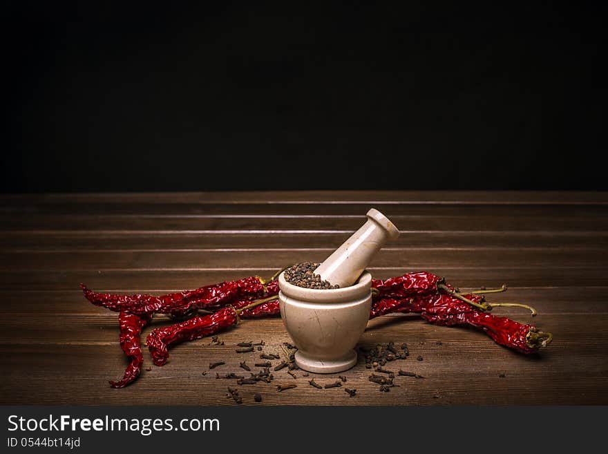 Marble mortar with spices black pepper, carnation and red hot pepper on a wooden table