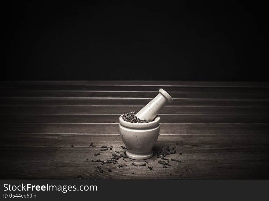 Marble mortar with spices black pepper and carnation on a wooden table