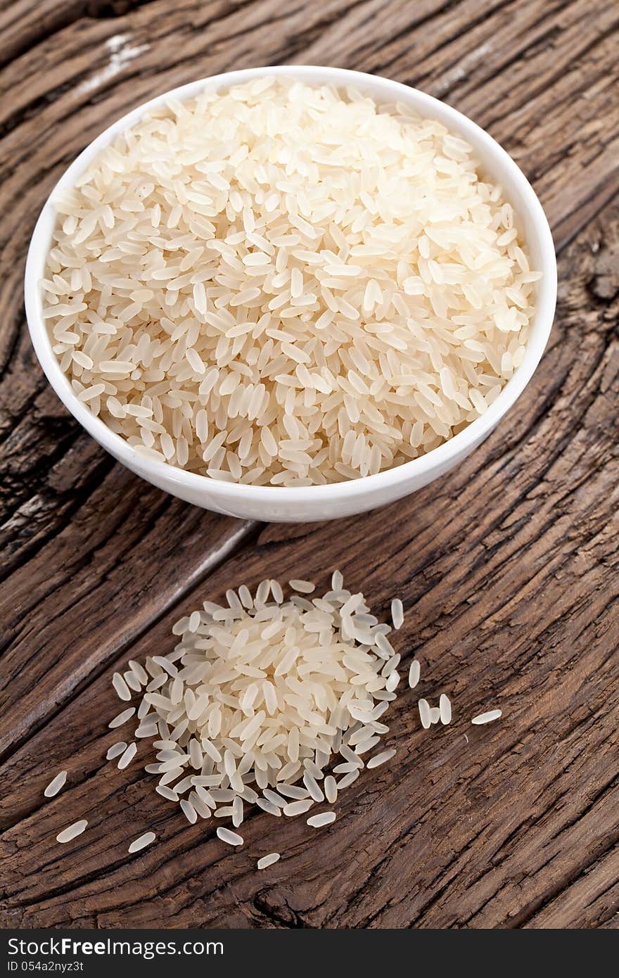 Uncooked rice in a bowl on a dark wooden table.