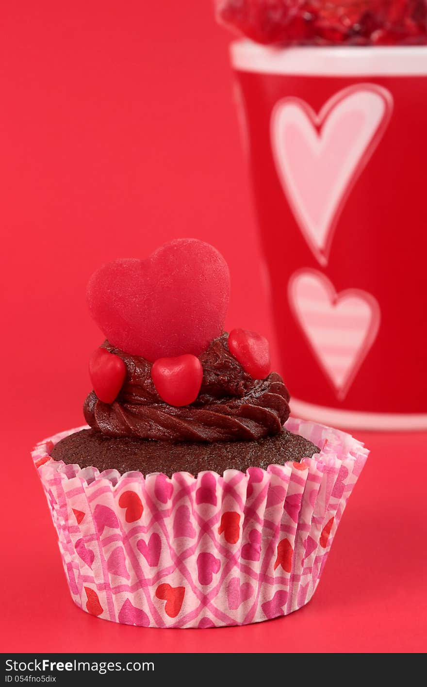 Moist chocolate cupcake with an icing swirl topped with candy hearts on red background. Moist chocolate cupcake with an icing swirl topped with candy hearts on red background