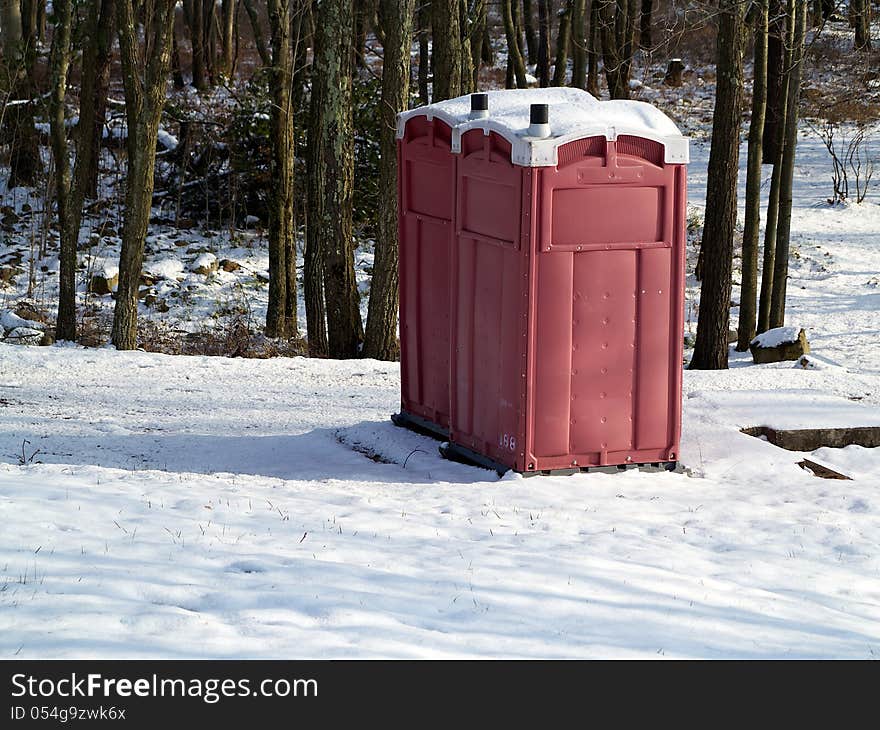 A pair of red outhouses sit in snow in a wintry forest. A pair of red outhouses sit in snow in a wintry forest.