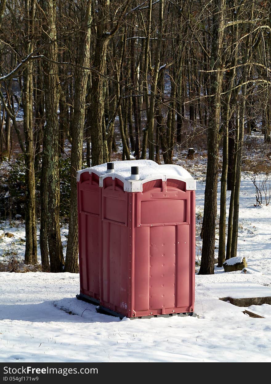 A pair of red outhouses sit in snow in a wintry forest. A pair of red outhouses sit in snow in a wintry forest.