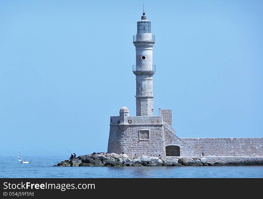 View of the lighthouse and a man fishing at the entrance to the harbor at Chania, Crete, Greece. View of the lighthouse and a man fishing at the entrance to the harbor at Chania, Crete, Greece.