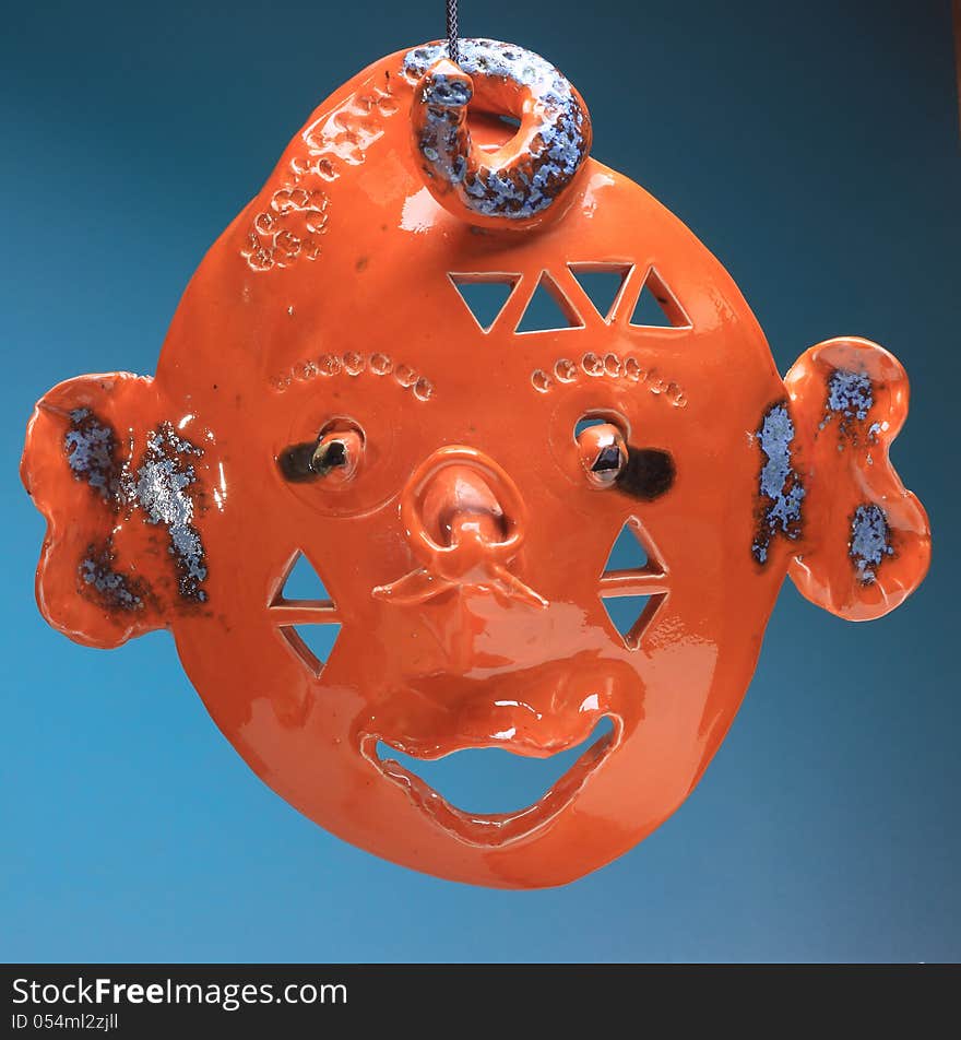 Face laughing made of ceramic which is glazed with deep orange color, background sea blue. Face laughing made of ceramic which is glazed with deep orange color, background sea blue.