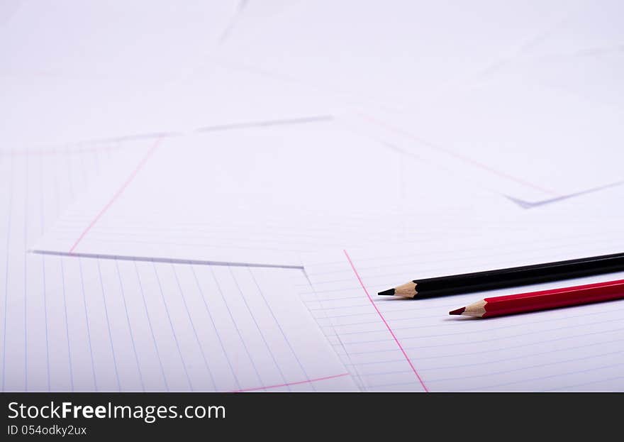 Black and red pencil exactly lie on a surface from writing-book sheets