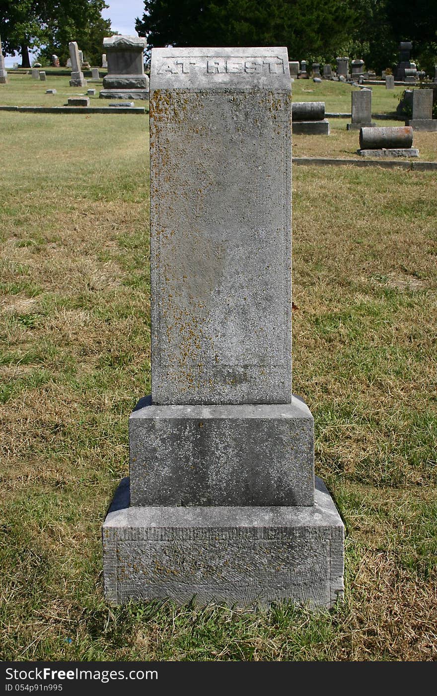 An old moss and lichen covered upright tombstone with the words At Rest on the top of the stone. An old moss and lichen covered upright tombstone with the words At Rest on the top of the stone.