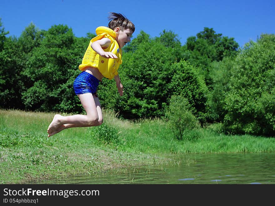 The little boy jumps from the shore into the water in life jacket. The little boy jumps from the shore into the water in life jacket