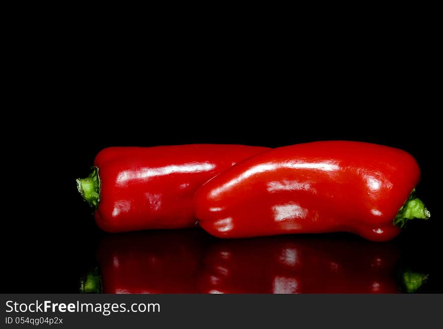 Two red peppers on black background with reflection