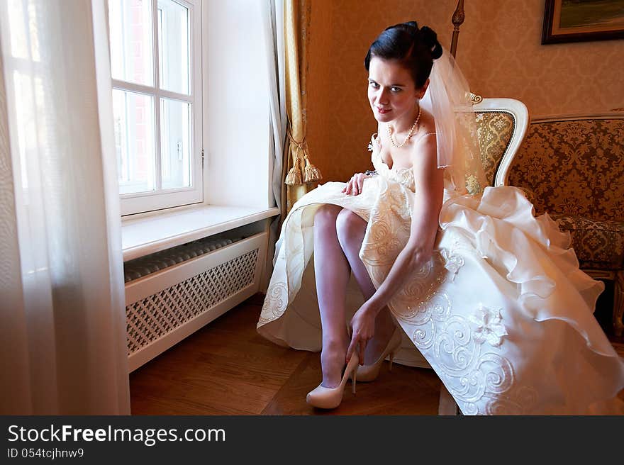 Happy bride wears her shoes and looking at camera