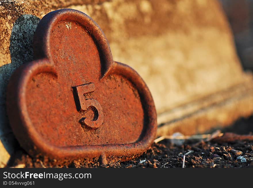 This is a closeup image of an antique rusty cast iron grave marker in a historical graveyard cementary in Kalbar, Queensland, Australia which was established in 1877. This graveyard and the grave markers as shown in this image are over 150 years old. It is made of heavy cast iron which is very rusty and has the appearance of a key head shape. It shows no name, just the number five 5. This is a closeup image of an antique rusty cast iron grave marker in a historical graveyard cementary in Kalbar, Queensland, Australia which was established in 1877. This graveyard and the grave markers as shown in this image are over 150 years old. It is made of heavy cast iron which is very rusty and has the appearance of a key head shape. It shows no name, just the number five 5.