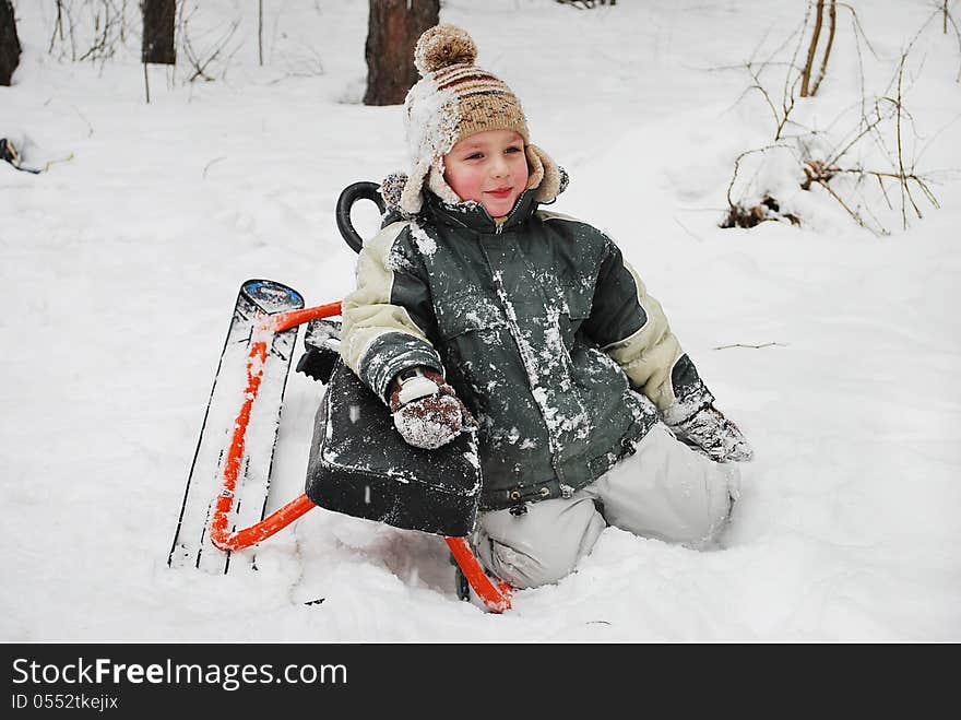 Boy sitting on snow with a sledge, winter cold day in the woods. Boy sitting on snow with a sledge, winter cold day in the woods.