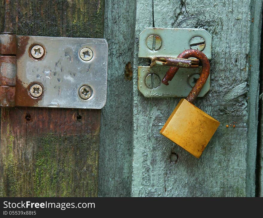 A rusty brass lock hangs on a steel hasp on a green door. A rusty brass lock hangs on a steel hasp on a green door