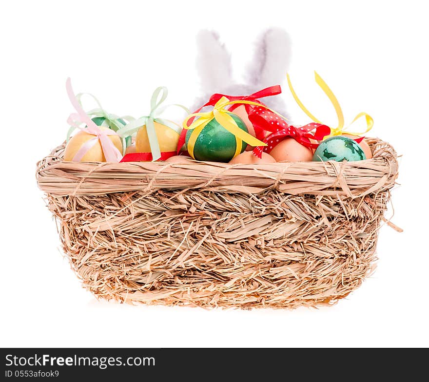 Rabbit looks out of the straw basket with Easter eggs on the white. Rabbit looks out of the straw basket with Easter eggs on the white