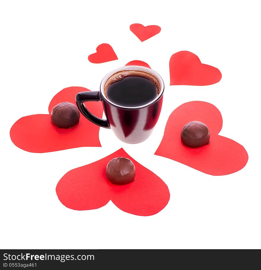 Round chocolate candy in the heart of red paper and black coffee on a white background. Round chocolate candy in the heart of red paper and black coffee on a white background