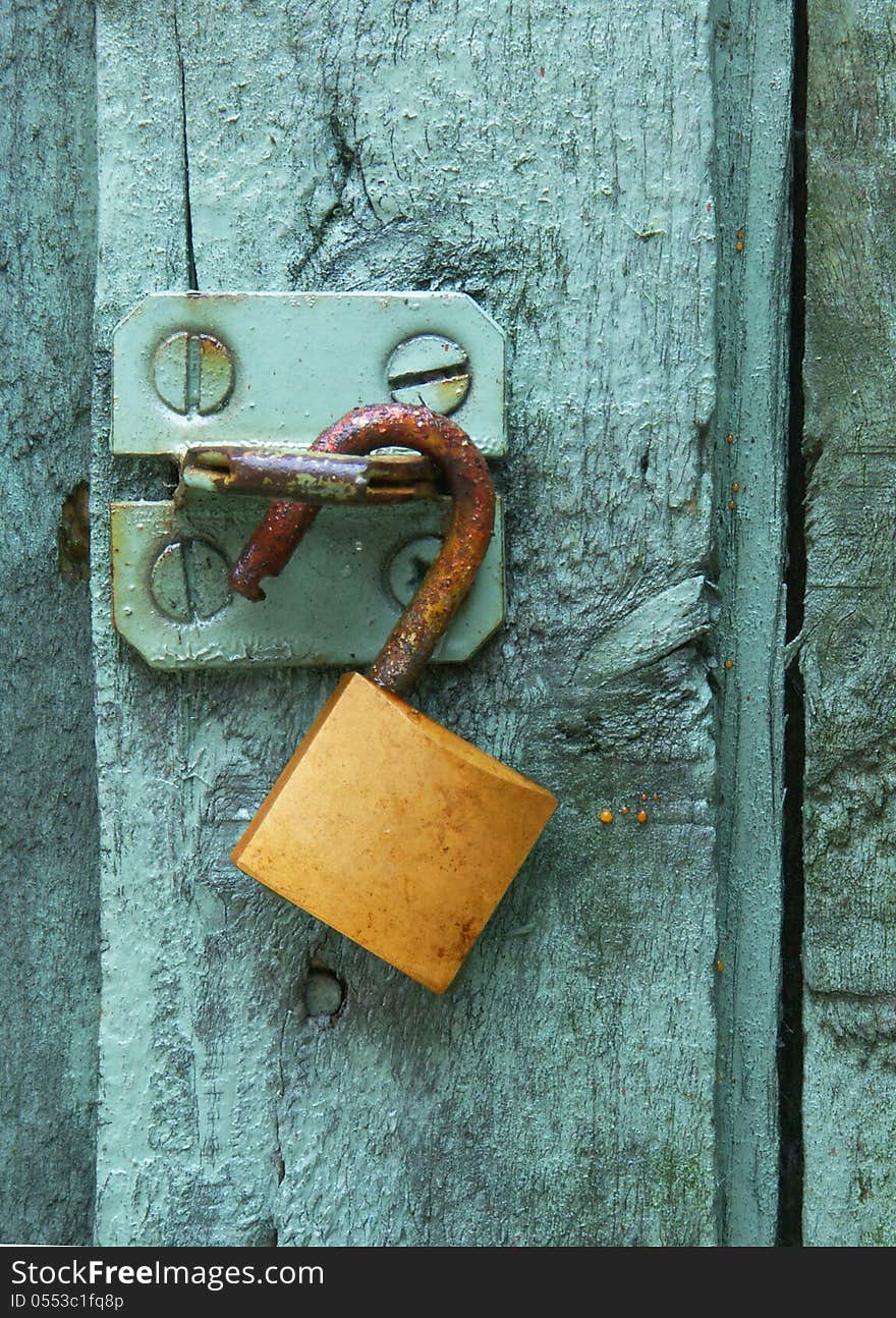 A rusty brass lock hangs on a steel hasp on a green door. A rusty brass lock hangs on a steel hasp on a green door