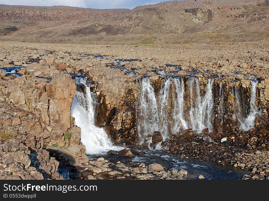 A Rocky Landscape With A Waterfall.