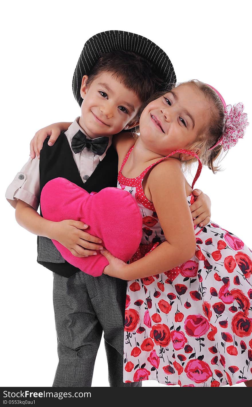 Smiley boy and girl are holding big pink heart beteen them.