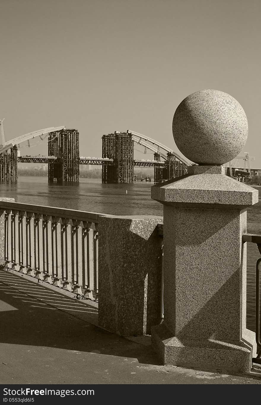 Granite ball on the background of the bridge being built across the River Dnipro in Kiev, Ukraine. Granite ball on the background of the bridge being built across the River Dnipro in Kiev, Ukraine