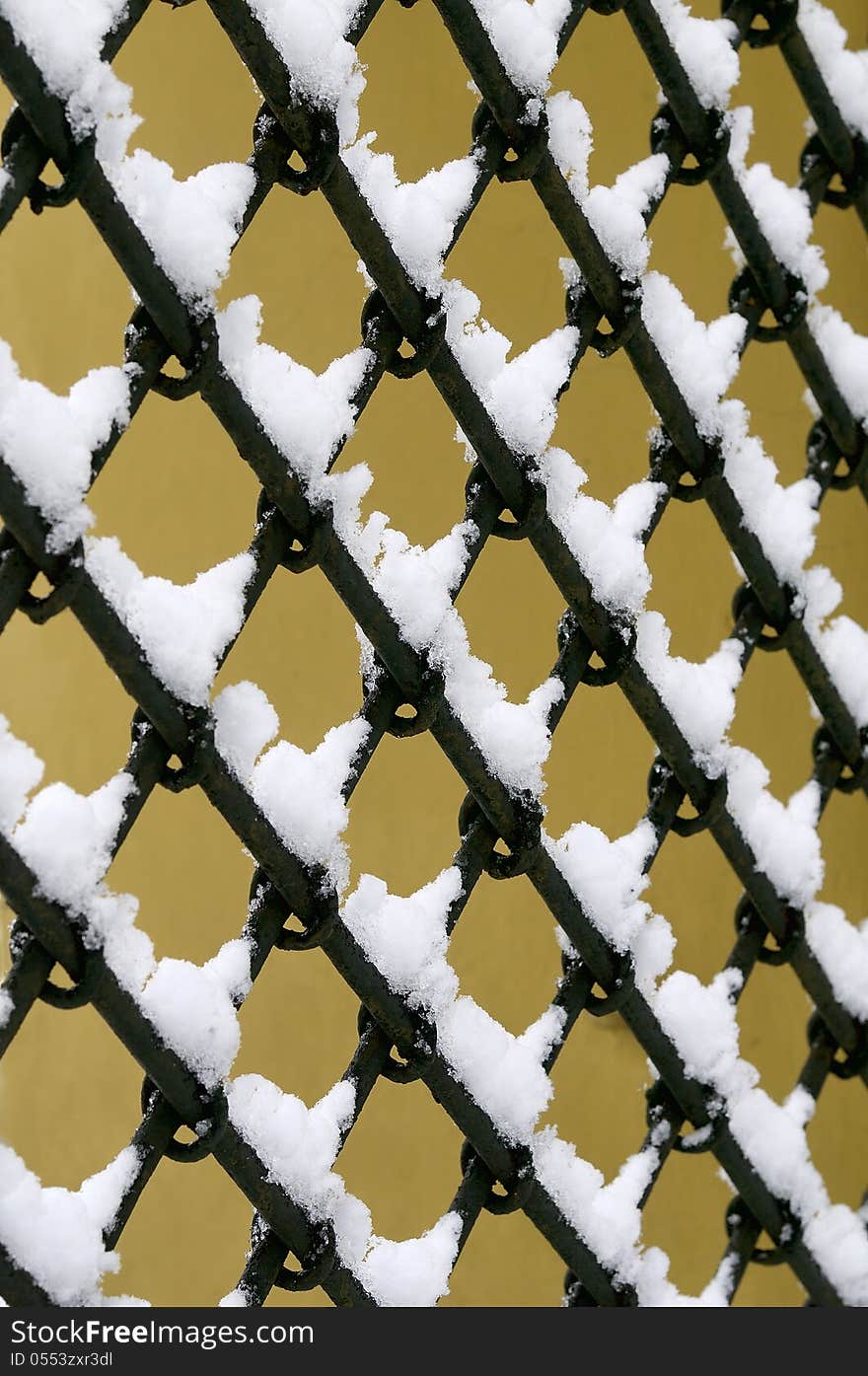 Old fashioned metal fence against yellow wall background covered in snow