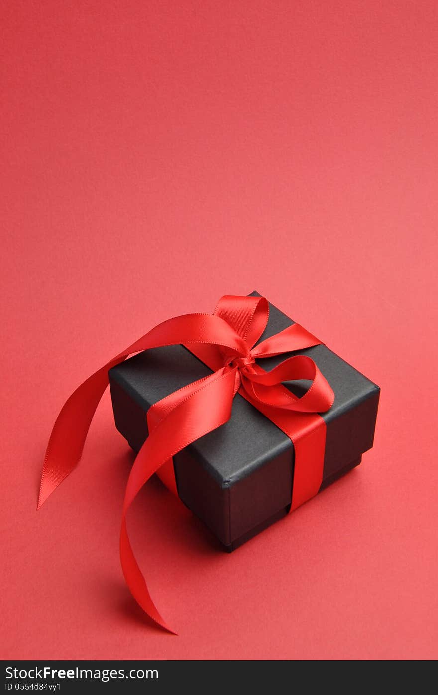 Beautiful Valentine black box gift present with red ribbon bow on a red background. Beautiful Valentine black box gift present with red ribbon bow on a red background.