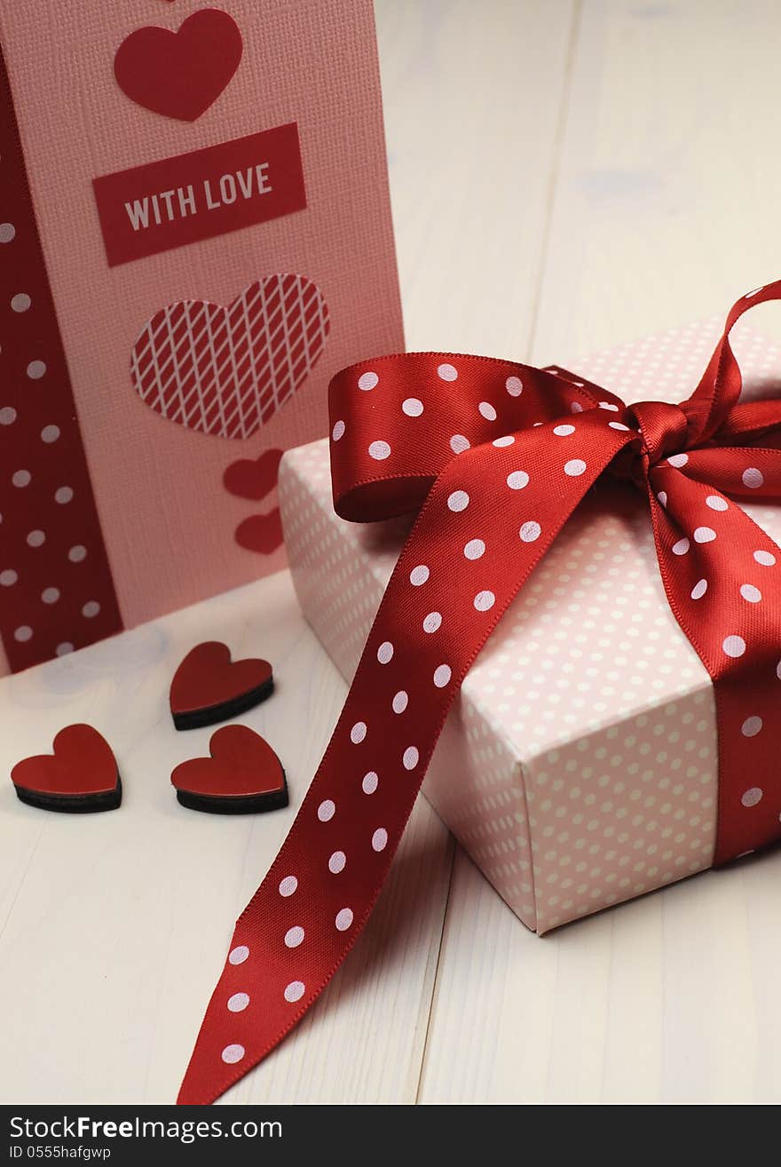 Handmade gift card with pink gift and red polka dot ribbon and heart on white natural wood table. Handmade gift card with pink gift and red polka dot ribbon and heart on white natural wood table.