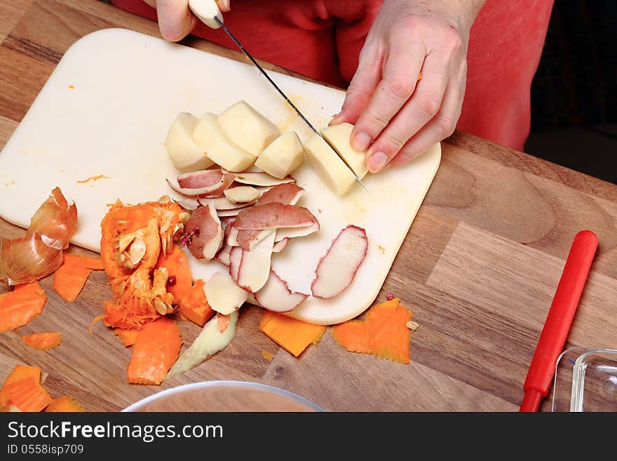 Making of a pumpkin soup: A potato is cut to pieces. On a worktop lie already the peels of it and the inner parts of a red pumpkin.