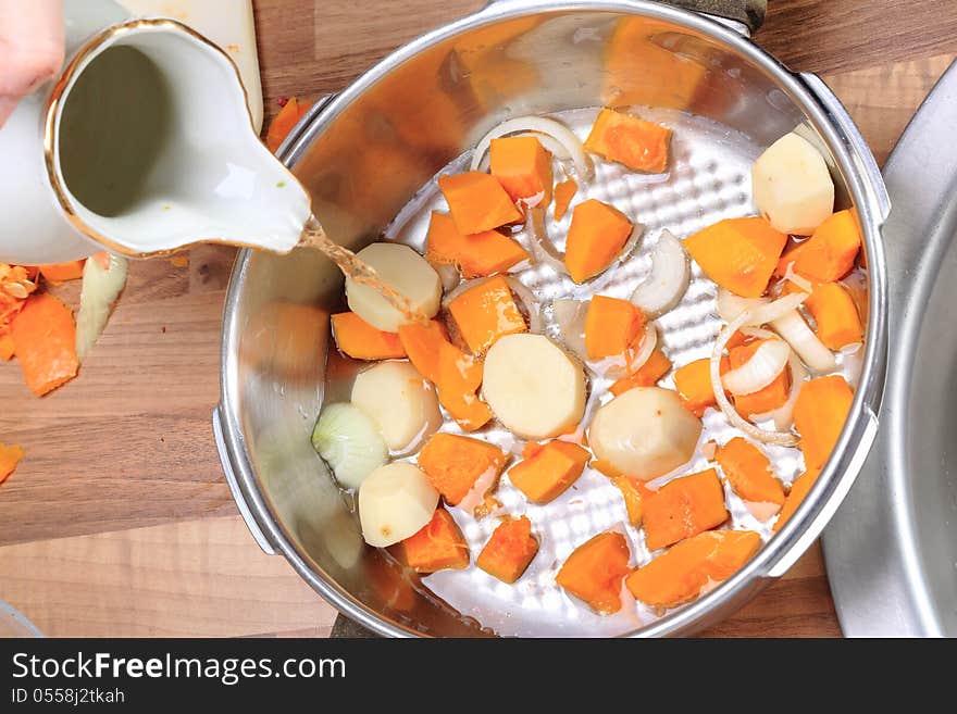 Making a pumpkin soup:Pieces of a red pumpkin and of potatoes with some slices of onion in a pressure cooker. Water is added. Making a pumpkin soup:Pieces of a red pumpkin and of potatoes with some slices of onion in a pressure cooker. Water is added.