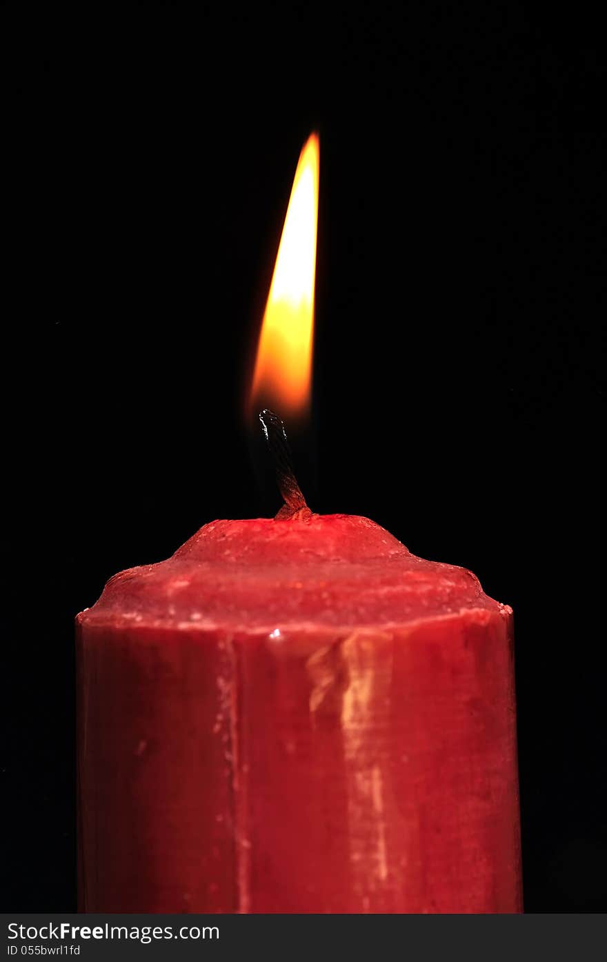 A single burning red candle isolated in front of black background