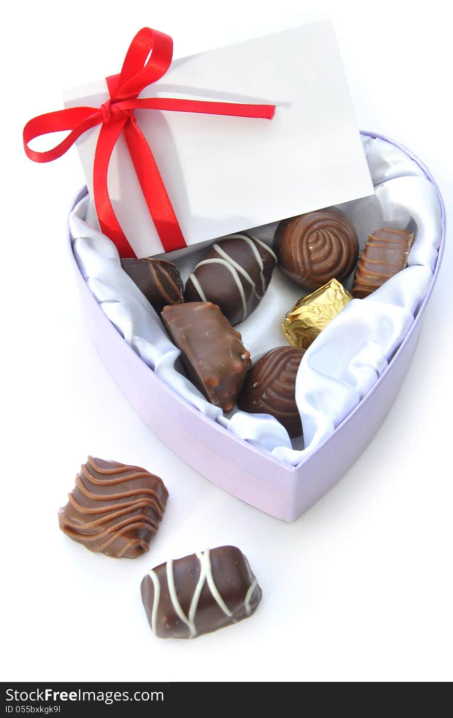Assortment of chocolates inside a heartshaped box with a card and decorative red ribbon. Assortment of chocolates inside a heartshaped box with a card and decorative red ribbon