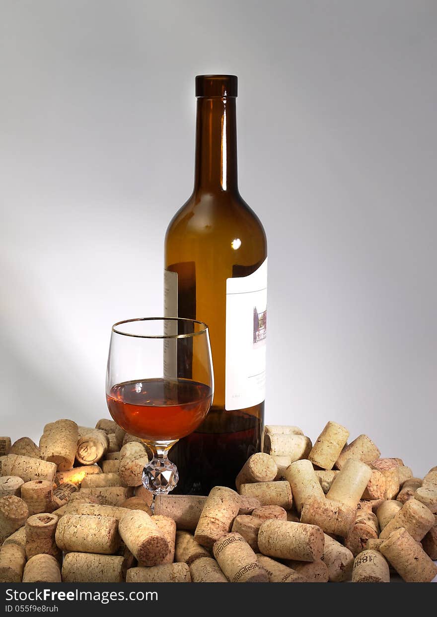 A glass of wine, a bottle, and many corks on a gray background