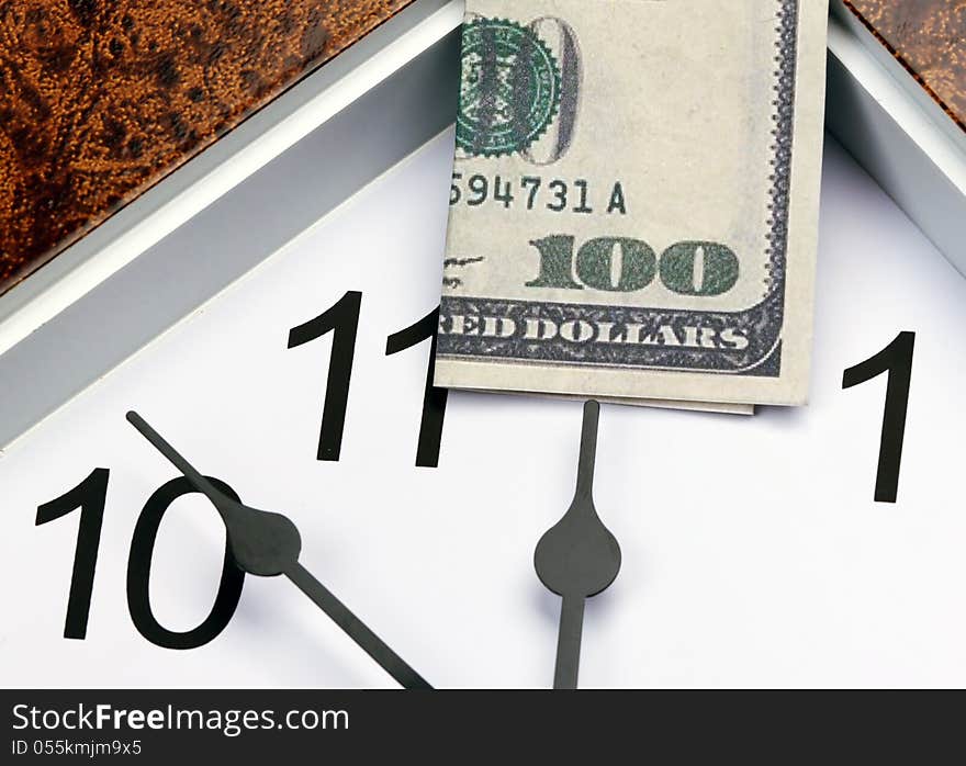 Time is money. hour hand points to the U.S. hundred dollar bill.