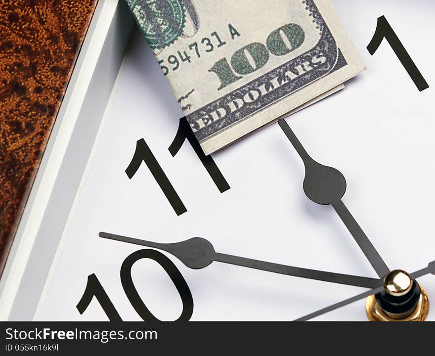 Time is money. hour hand points to the U.S. hundred dollar bill.