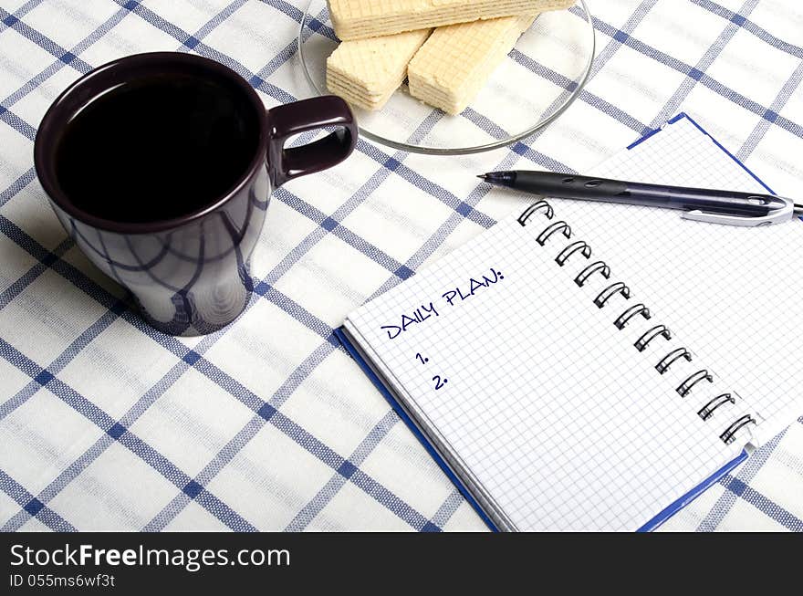 Notebook on a table next to a cup of coffee and a plate of cookies