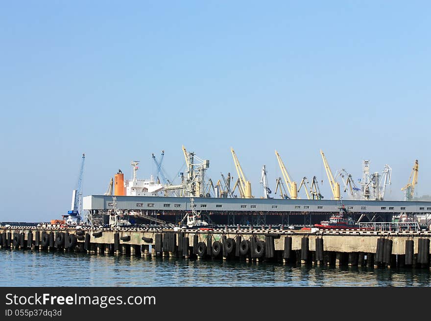 Port berth with material handling equipment and cargo ships at anchor. Port berth with material handling equipment and cargo ships at anchor